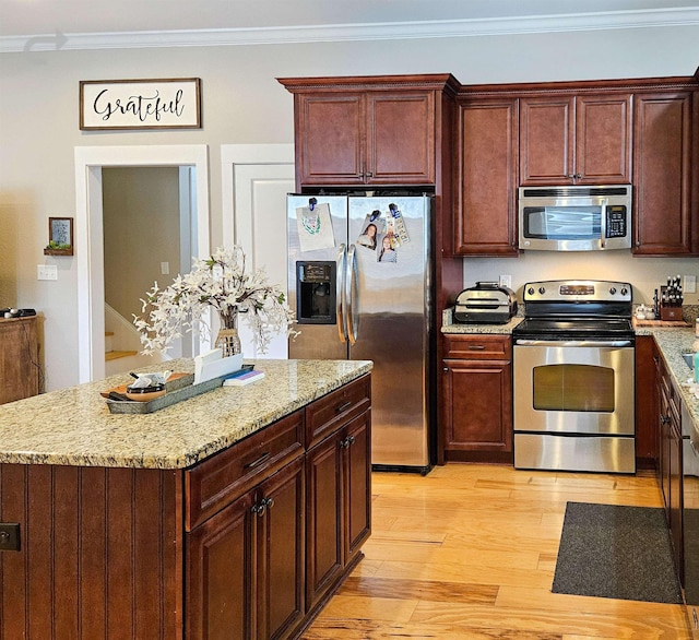 kitchen featuring light hardwood / wood-style flooring, ornamental molding, a kitchen island, stainless steel appliances, and light stone countertops