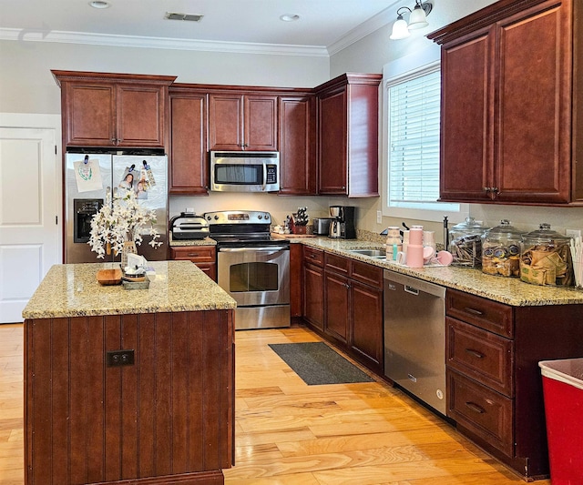 kitchen with crown molding, light stone counters, light wood-type flooring, appliances with stainless steel finishes, and a kitchen island