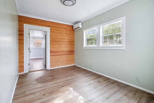 empty room featuring a healthy amount of sunlight, a wall mounted air conditioner, baseboards, and wood finished floors