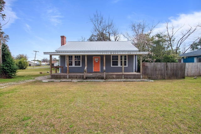 view of front of property featuring metal roof, a porch, fence, a chimney, and a front yard