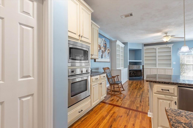 kitchen with light hardwood / wood-style flooring, a textured ceiling, stainless steel appliances, hanging light fixtures, and cream cabinets