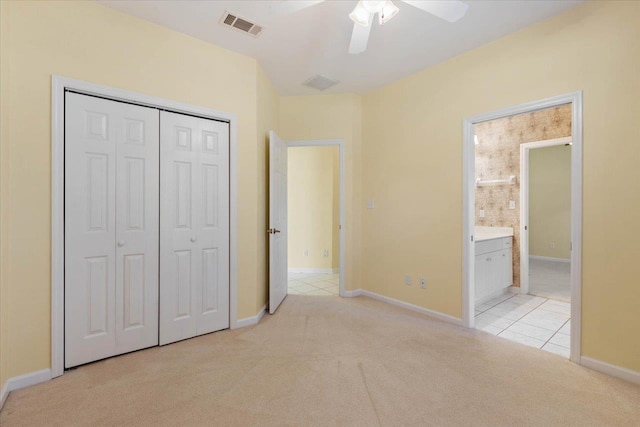 unfurnished bedroom featuring ceiling fan, light carpet, a closet, and ensuite bathroom