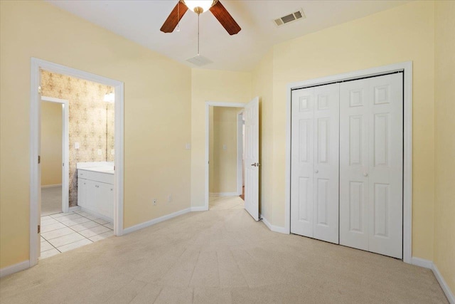 unfurnished bedroom with a closet, connected bathroom, light colored carpet, and ceiling fan