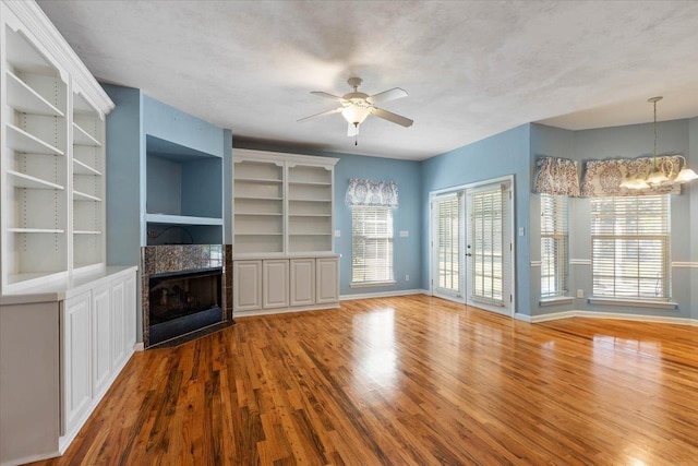 unfurnished living room with ceiling fan with notable chandelier, a tile fireplace, built in shelves, and hardwood / wood-style floors