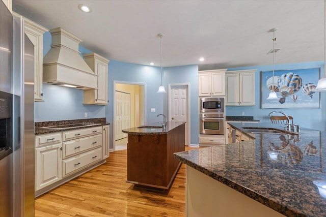 kitchen with stainless steel appliances, sink, dark stone counters, custom exhaust hood, and pendant lighting