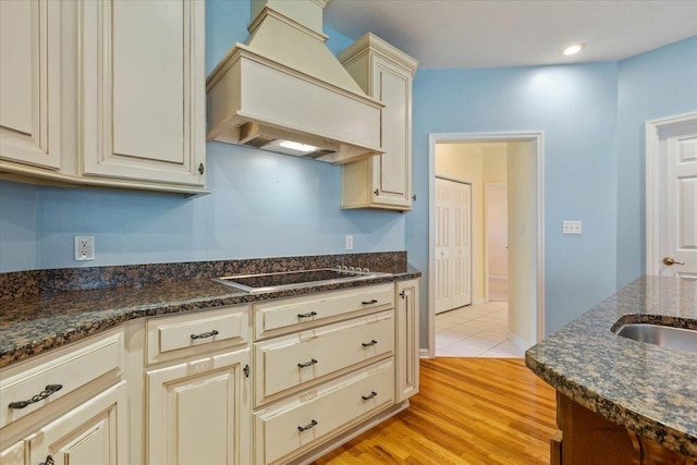 kitchen featuring stovetop, premium range hood, dark stone counters, light hardwood / wood-style floors, and cream cabinets