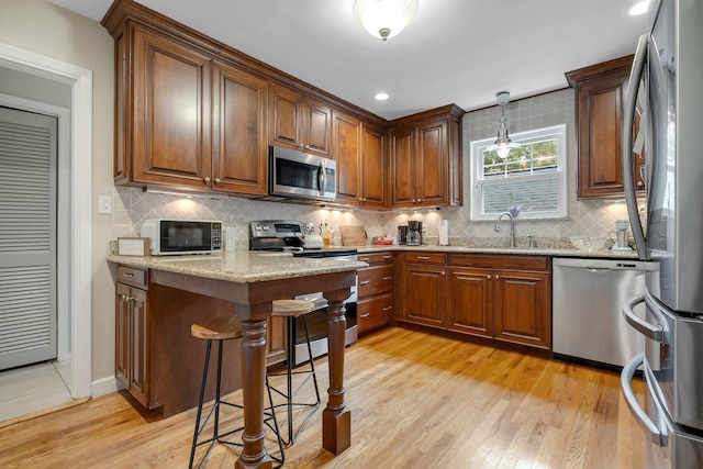 kitchen featuring stainless steel appliances, a sink, decorative backsplash, light wood-style flooring, and recessed lighting