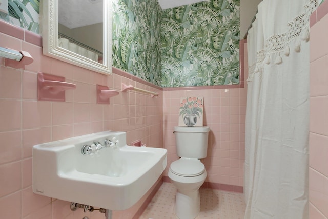 full bathroom featuring wallpapered walls, a sink, a wainscoted wall, toilet, and tile walls