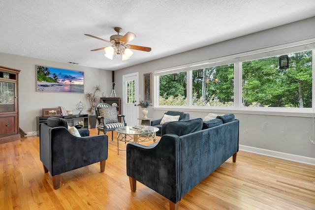 living area with ceiling fan, a textured ceiling, healthy amount of natural light, light wood-type flooring, and baseboards