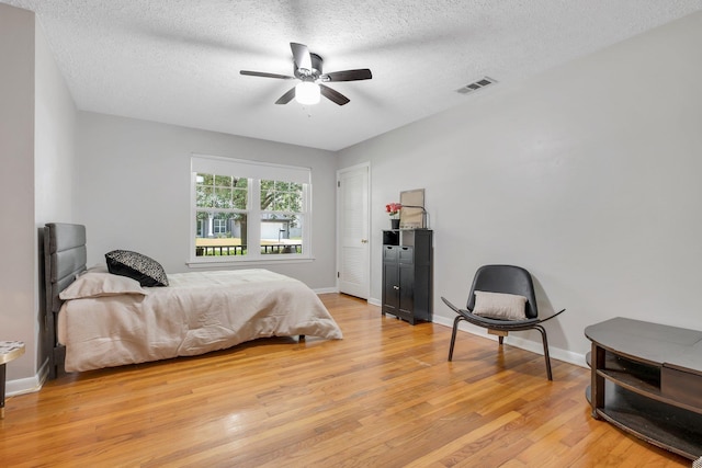 bedroom with light wood finished floors, a textured ceiling, baseboards, and a ceiling fan