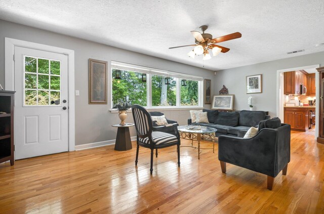 living room with a textured ceiling, ceiling fan, light wood finished floors, and baseboards