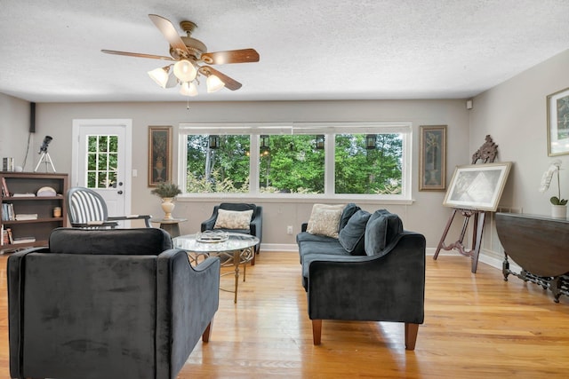 living area with light wood finished floors, a textured ceiling, a ceiling fan, and baseboards