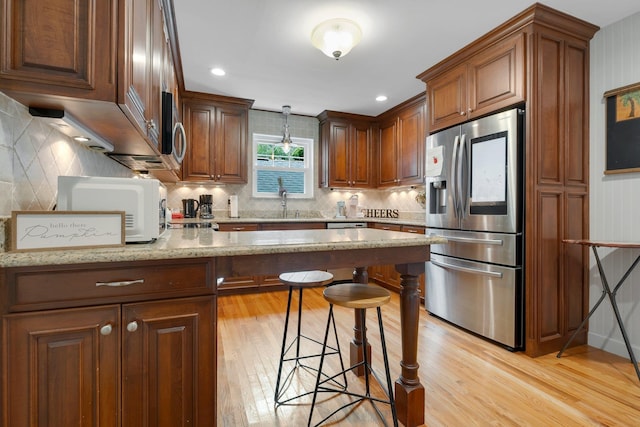 kitchen featuring stainless steel appliances, light wood-type flooring, a kitchen breakfast bar, light stone countertops, and decorative backsplash