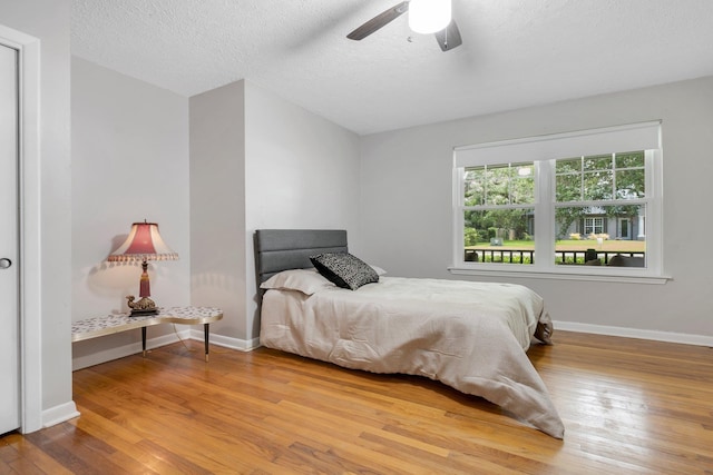 bedroom with wood finished floors, baseboards, a textured ceiling, and a ceiling fan