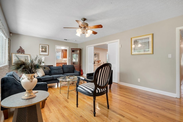 living area featuring a ceiling fan, light wood-style flooring, baseboards, healthy amount of natural light, and a textured ceiling
