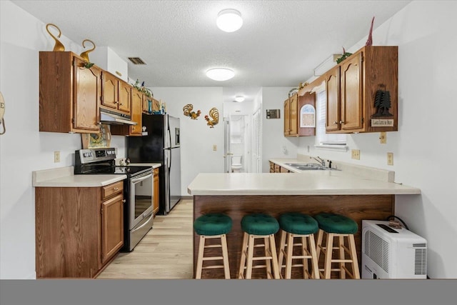 kitchen featuring stainless steel appliances, kitchen peninsula, a breakfast bar area, a textured ceiling, and light hardwood / wood-style flooring