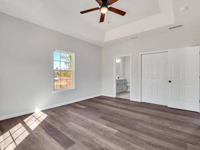 unfurnished bedroom featuring dark wood-type flooring, a raised ceiling, ceiling fan, connected bathroom, and a closet