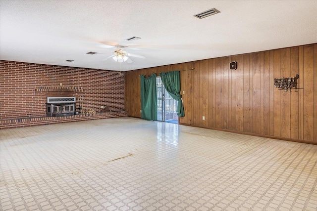 unfurnished living room with visible vents, brick wall, ceiling fan, heating unit, and a textured ceiling