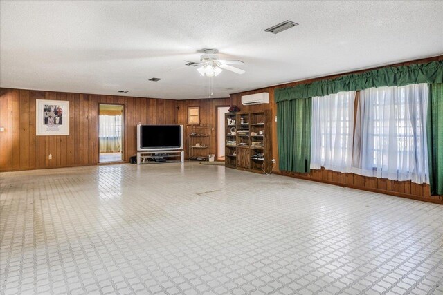 unfurnished living room with visible vents, wood walls, a wall unit AC, tile patterned floors, and a textured ceiling