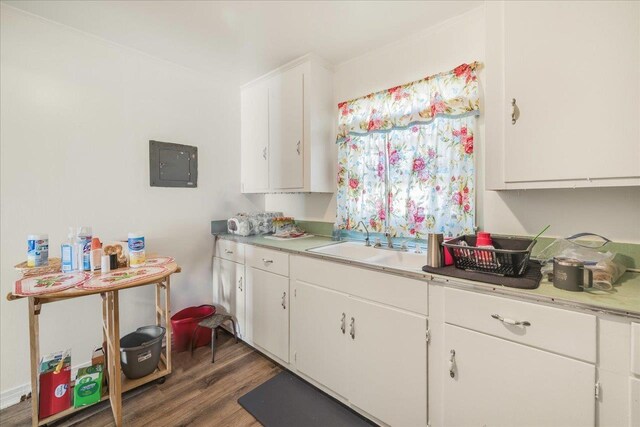 kitchen with electric panel, white cabinets, light countertops, and wood finished floors