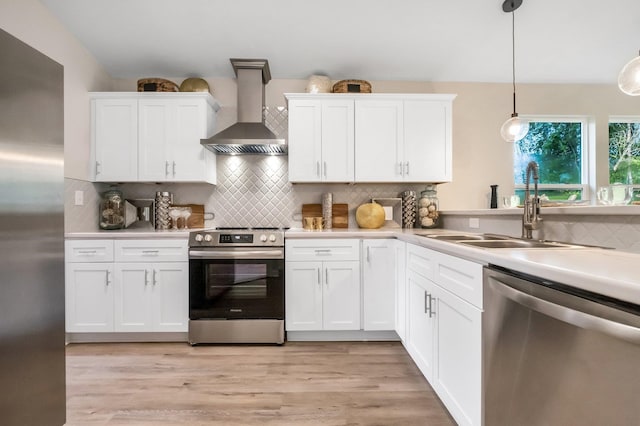 kitchen featuring hanging light fixtures, wall chimney exhaust hood, appliances with stainless steel finishes, and white cabinets