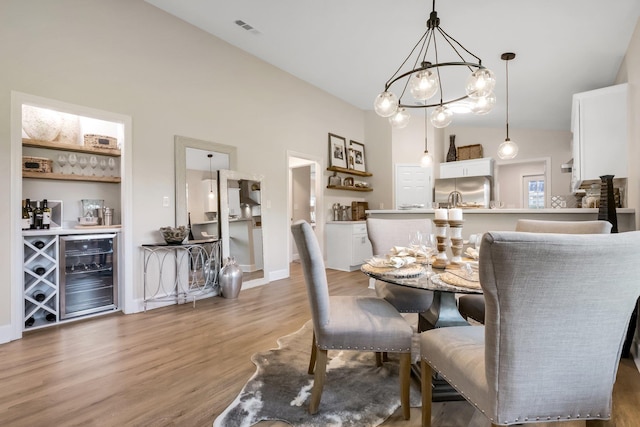 dining area with beverage cooler, visible vents, wood finished floors, an inviting chandelier, and high vaulted ceiling