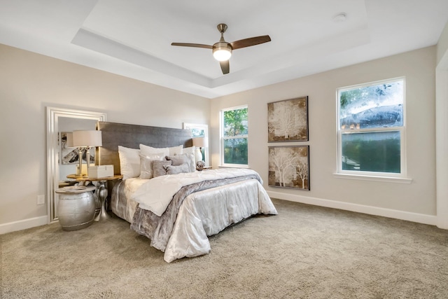 bedroom featuring carpet, a tray ceiling, ceiling fan, and baseboards