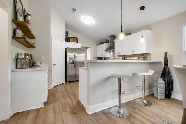 kitchen with light wood-style flooring, a peninsula, white cabinets, stainless steel fridge with ice dispenser, and decorative light fixtures