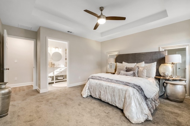 carpeted bedroom featuring visible vents, baseboards, a raised ceiling, connected bathroom, and ceiling fan