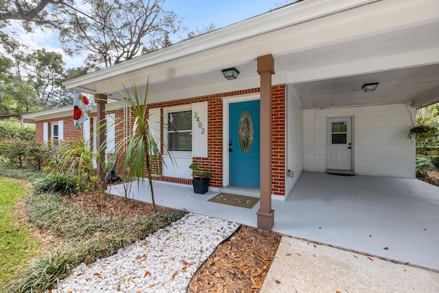 property entrance with a porch, an attached carport, and brick siding