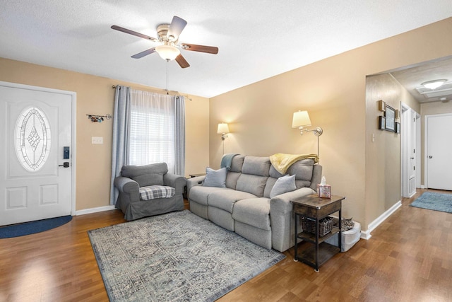 living room with ceiling fan, a textured ceiling, baseboards, and wood finished floors