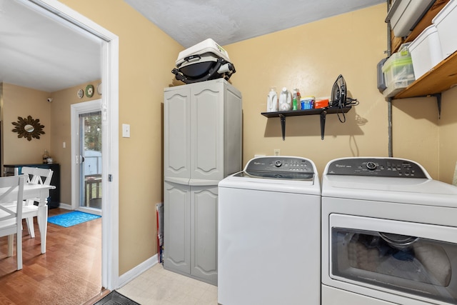 washroom featuring cabinet space, baseboards, washer and clothes dryer, and light floors