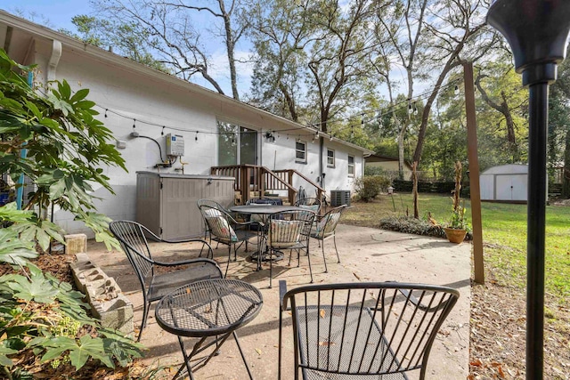 view of patio / terrace with outdoor dining space, a shed, central AC unit, and an outbuilding