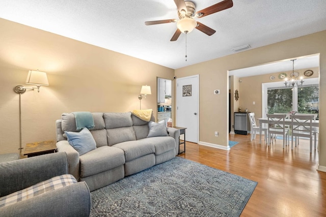 living room with a textured ceiling, ceiling fan with notable chandelier, wood finished floors, visible vents, and baseboards