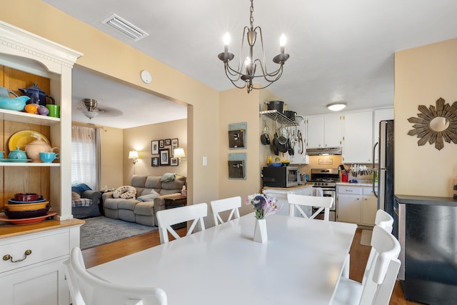 dining area featuring ceiling fan with notable chandelier, visible vents, and wood finished floors