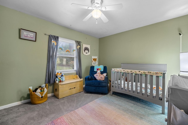 bedroom featuring carpet floors, a nursery area, ceiling fan, and baseboards