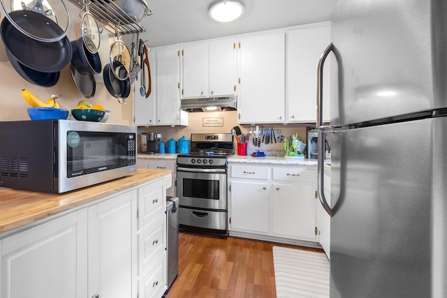 kitchen featuring under cabinet range hood, stainless steel appliances, light countertops, and wood finished floors