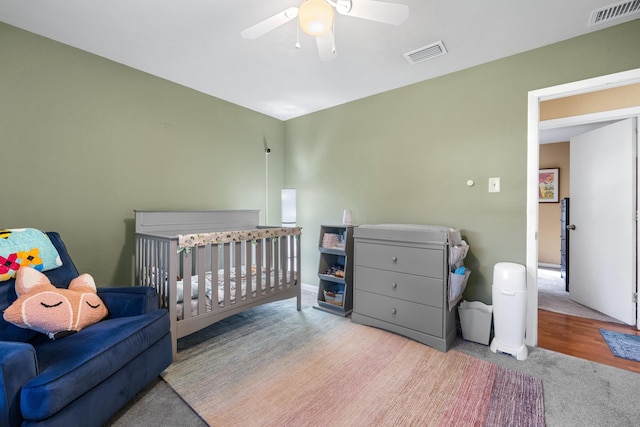 bedroom with a crib, carpet floors, ceiling fan, and visible vents