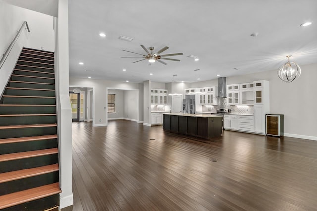 unfurnished living room featuring dark wood-type flooring, beverage cooler, and ceiling fan with notable chandelier