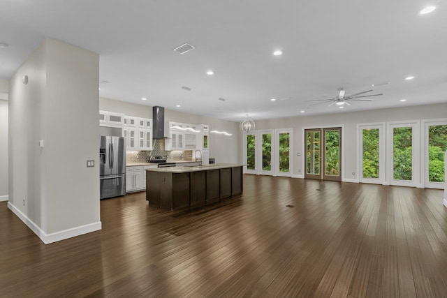 kitchen with backsplash, dark hardwood / wood-style flooring, a kitchen island with sink, stainless steel appliances, and wall chimney exhaust hood