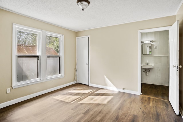 unfurnished bedroom with connected bathroom, sink, a textured ceiling, a closet, and hardwood / wood-style floors