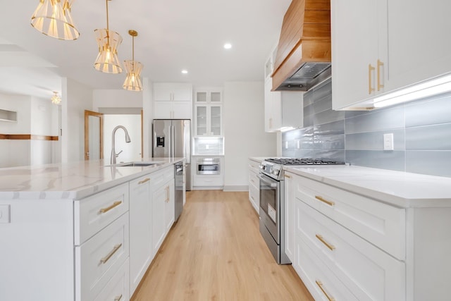 kitchen with sink, a center island with sink, white cabinets, custom range hood, and appliances with stainless steel finishes