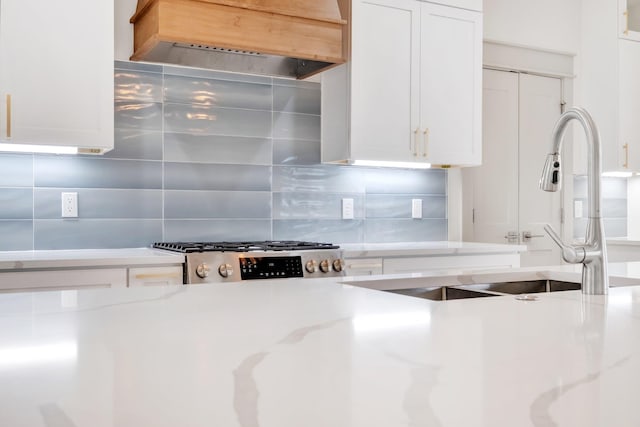 kitchen with decorative backsplash, ventilation hood, sink, white cabinets, and range