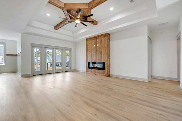 unfurnished living room with ceiling fan, a large fireplace, a raised ceiling, and light wood-type flooring