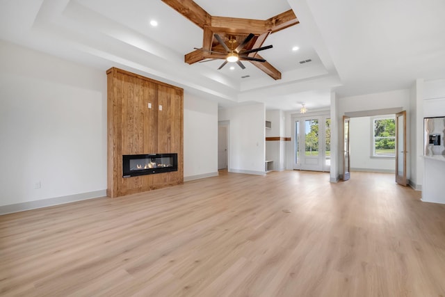 unfurnished living room featuring coffered ceiling, a raised ceiling, ceiling fan, light wood-type flooring, and a large fireplace