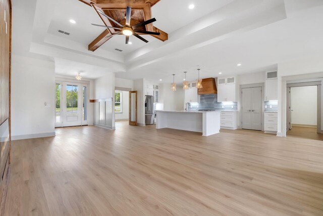 unfurnished living room featuring a raised ceiling, sink, and light hardwood / wood-style floors