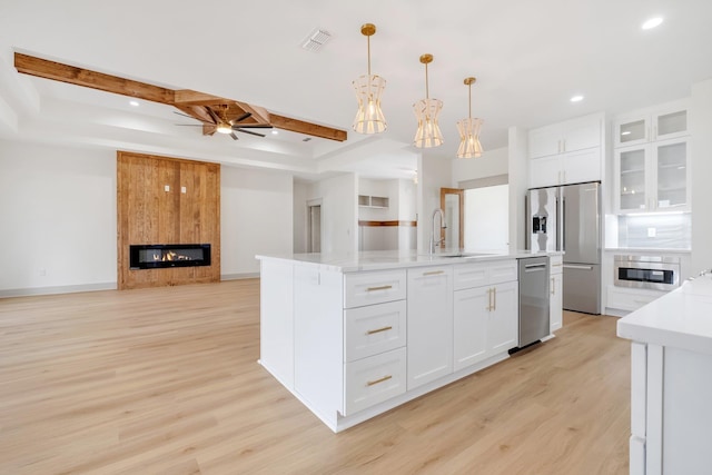 kitchen with white cabinets, a center island with sink, hanging light fixtures, and a fireplace