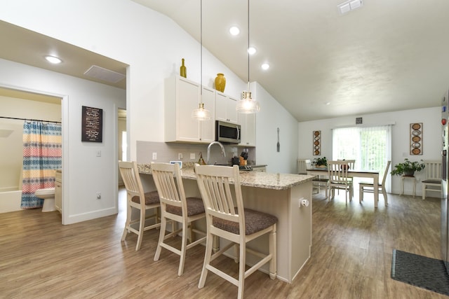 359 Mae Cato Dr, Midway, FL 32343 - kitchen featuring stainless steel microwave, vaulted ceiling, light wood-type flooring, light stone countertops, and a peninsula