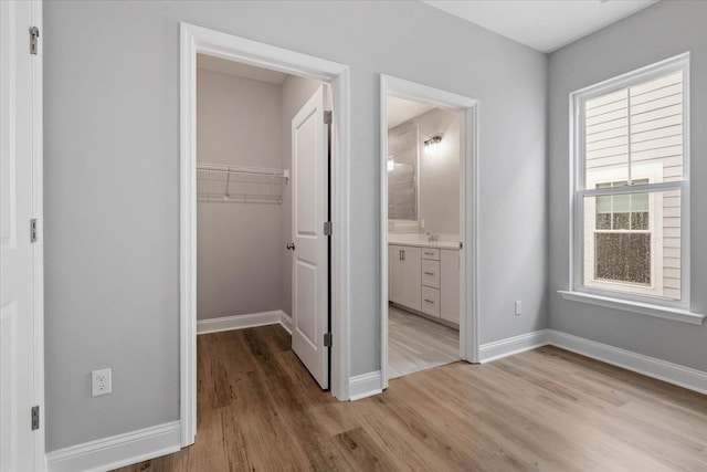 unfurnished bedroom with ensuite bathroom, a walk in closet, light wood-type flooring, and a closet