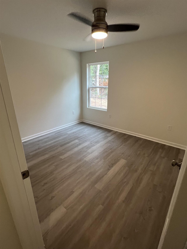 unfurnished room with dark wood-style floors, a ceiling fan, and baseboards